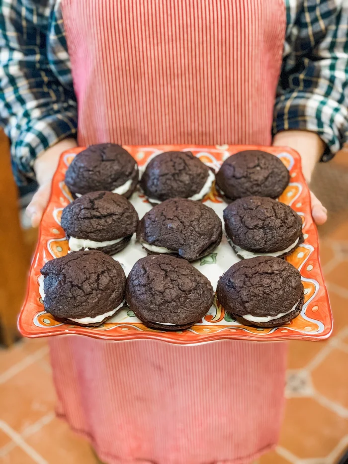 A tray of chocolate whoopie pies with cream filling on a pink cake stand.